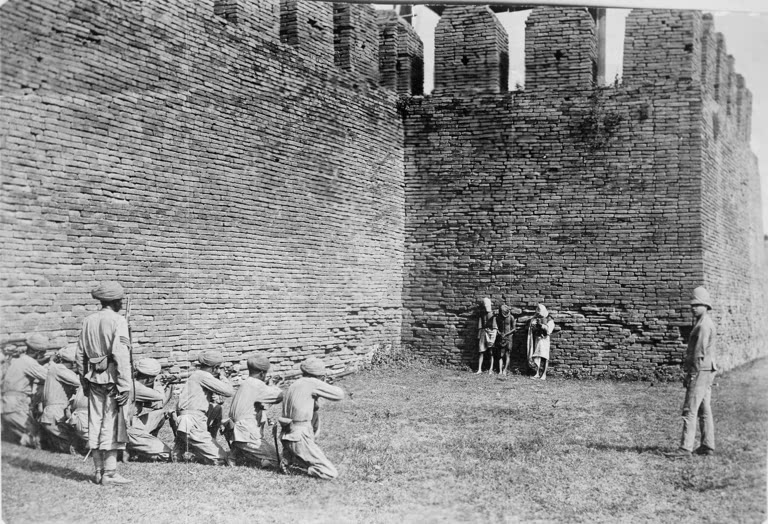 Execution of Burmese dacoits at Mandalay. A glass copy negative of a print showing three Burmese dacoits about to be executed by a British firing squad in front of the walls of Mandalay